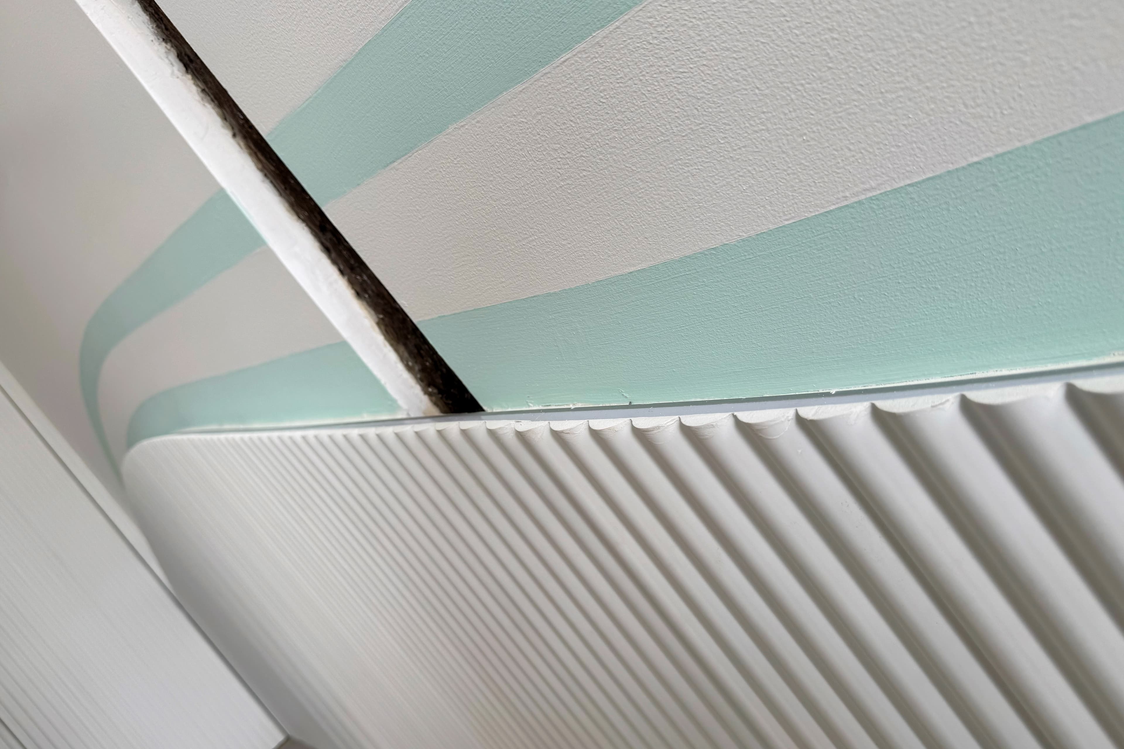 Primer plano de revestimiento acanalado blanco y composición mural de líneas curvas en tonos menta, destacando texturas y acabados del diseño interior de la clínica dental.
