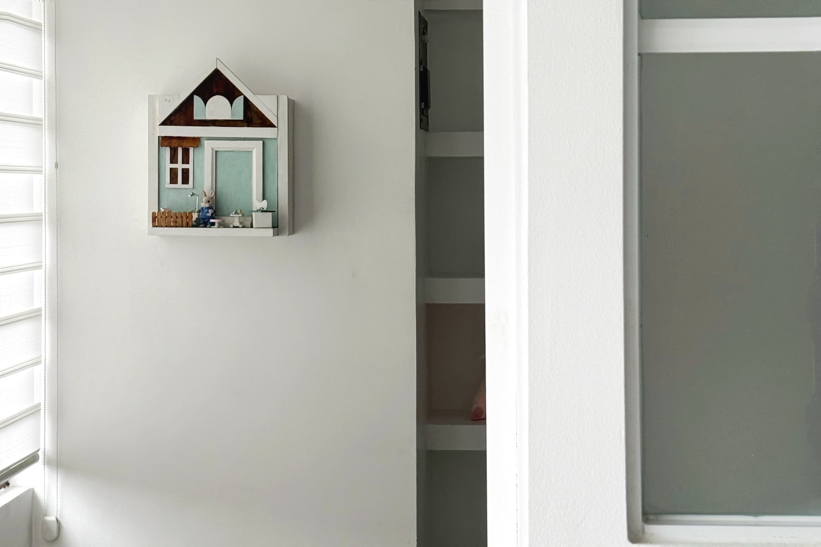 Detalle de decoración infantil en consultorio odontológico con una pequeña casa de madera en tonos menta, paredes blancas y estanterías integradas.